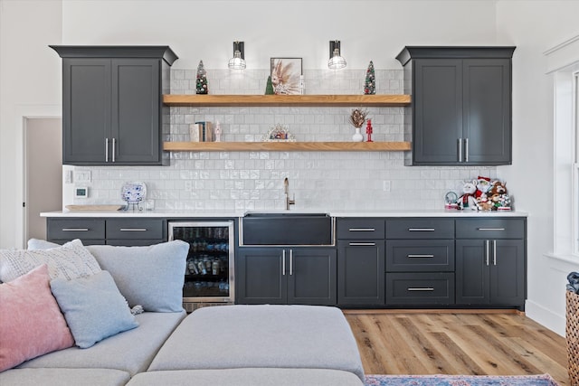 bar featuring light wood-type flooring, tasteful backsplash, beverage cooler, and sink