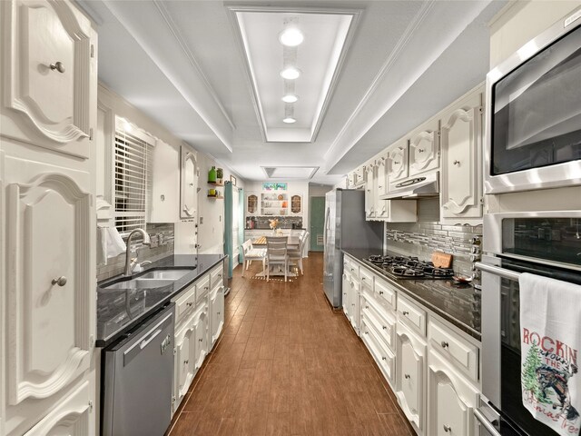 kitchen with stainless steel appliances, a tray ceiling, dark wood-type flooring, sink, and white cabinets