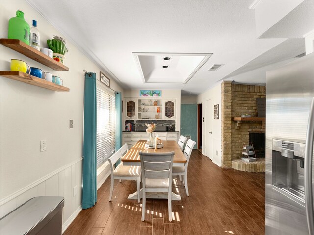 dining area featuring a raised ceiling, ornamental molding, dark wood-type flooring, and a brick fireplace