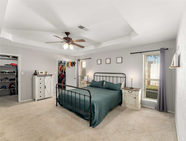 carpeted bedroom with a raised ceiling, a spacious closet, and ceiling fan