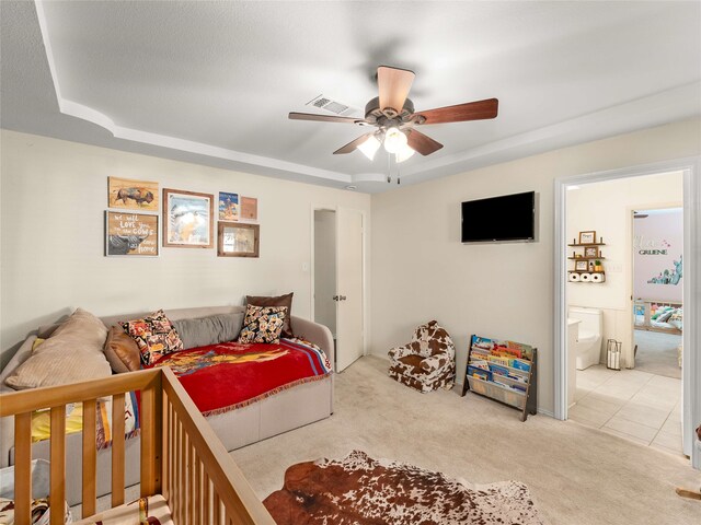 bedroom featuring light carpet, ensuite bath, a textured ceiling, a raised ceiling, and ceiling fan