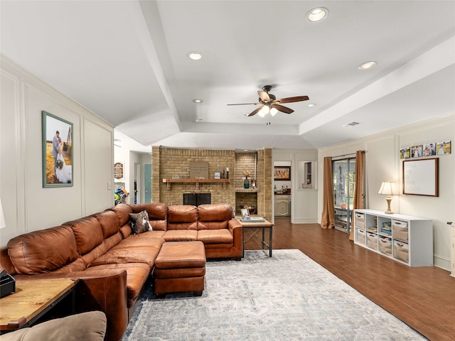 living room featuring a tray ceiling, ceiling fan, a fireplace, and dark wood-type flooring