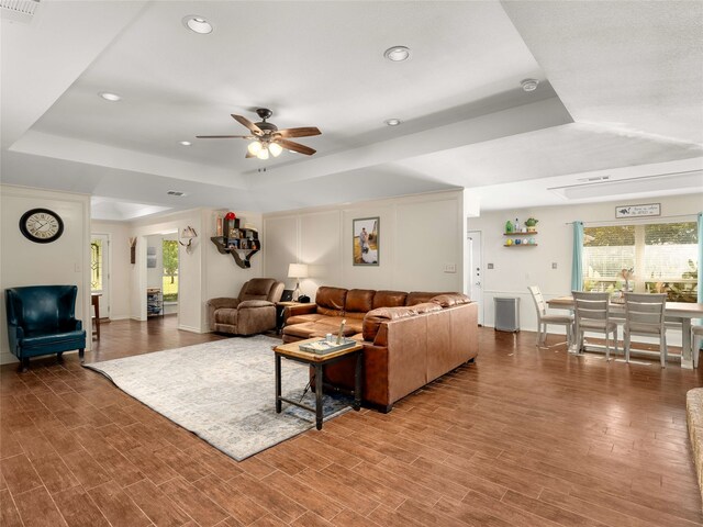 living room with hardwood / wood-style floors, a tray ceiling, and ceiling fan