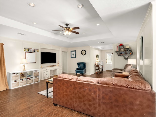 living room with dark hardwood / wood-style floors, ceiling fan, and a tray ceiling