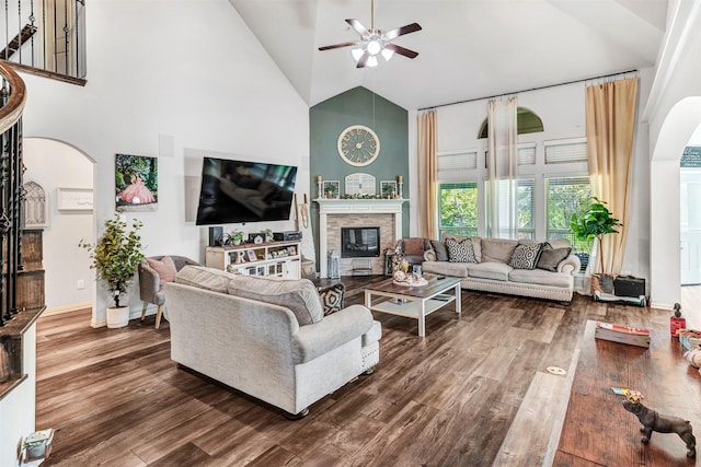 living room with ceiling fan, a stone fireplace, hardwood / wood-style floors, and high vaulted ceiling