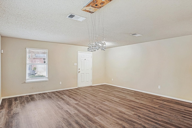 unfurnished room featuring dark hardwood / wood-style flooring, a textured ceiling, and an inviting chandelier