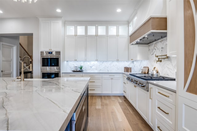 kitchen with custom exhaust hood, light stone countertops, white cabinetry, and stainless steel appliances