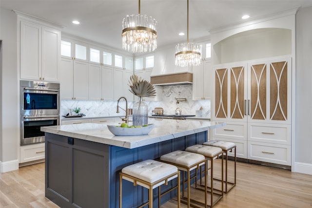 kitchen featuring appliances with stainless steel finishes, light wood-type flooring, light stone counters, a kitchen island with sink, and white cabinetry