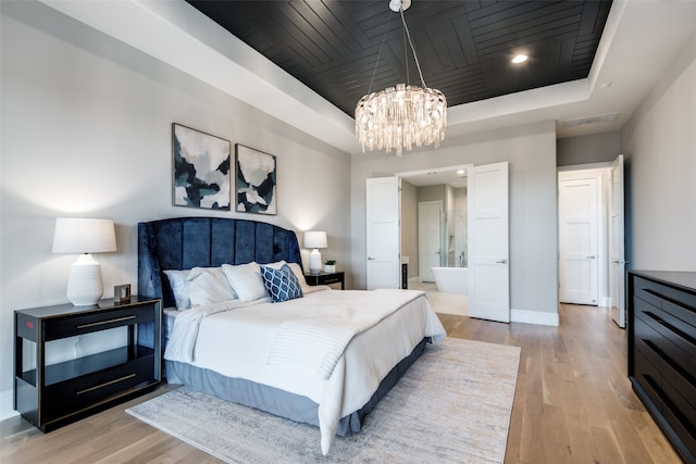 bedroom featuring light hardwood / wood-style floors, an inviting chandelier, connected bathroom, and a tray ceiling