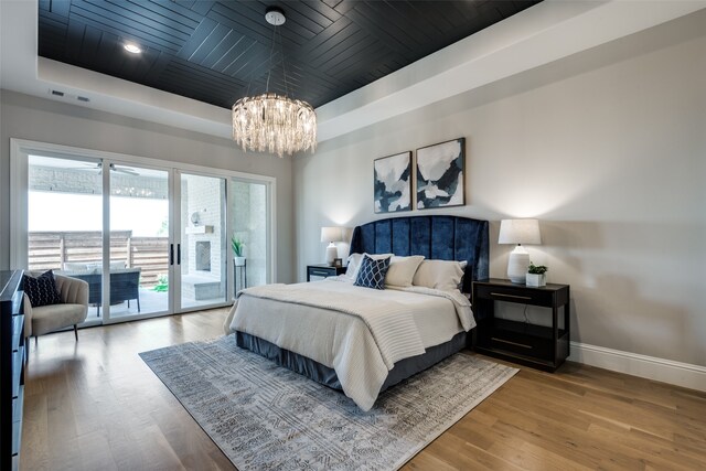 bedroom with access to outside, a raised ceiling, wood-type flooring, an inviting chandelier, and wooden ceiling