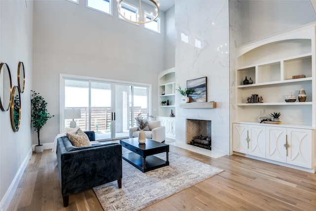 living room with built in shelves, a premium fireplace, light hardwood / wood-style flooring, and a towering ceiling