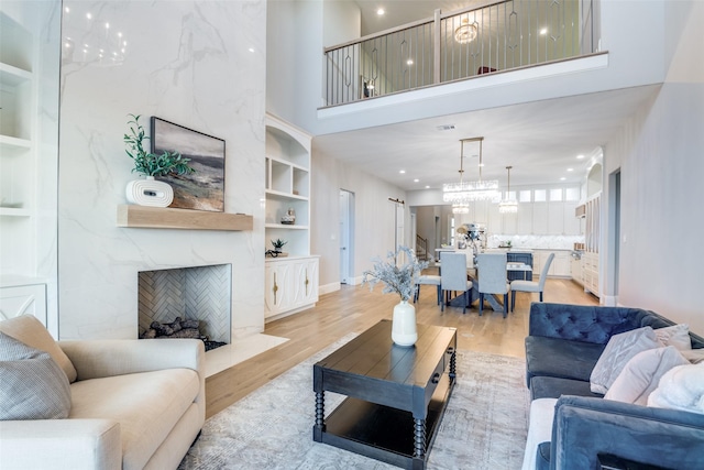 living room featuring a towering ceiling, built in shelves, light wood-type flooring, and a premium fireplace