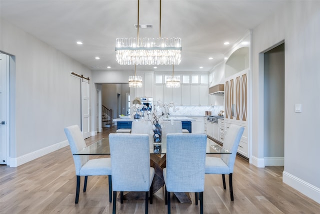 dining area featuring a barn door, light hardwood / wood-style flooring, and an inviting chandelier