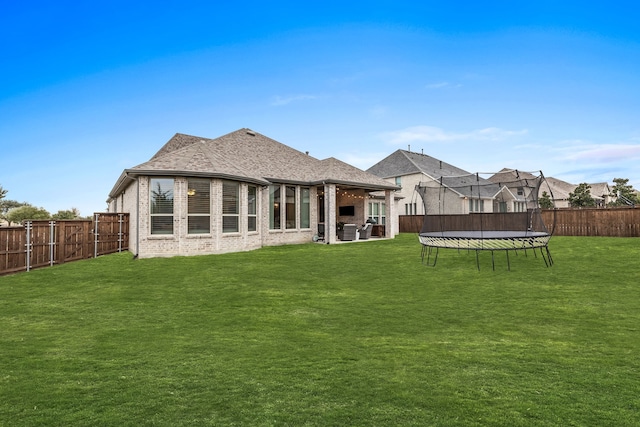 rear view of house featuring a trampoline and a yard