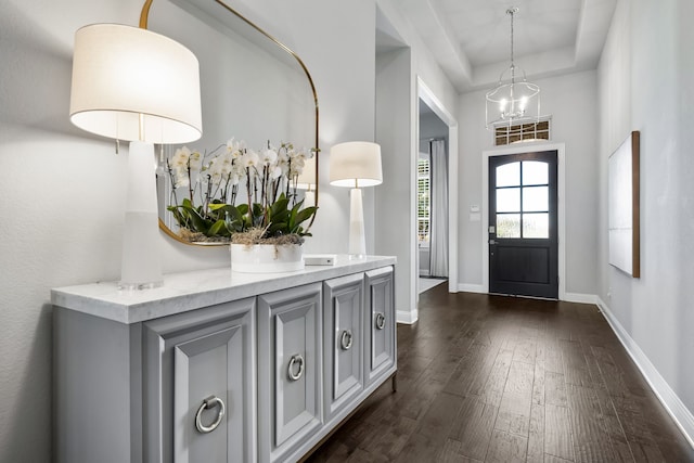 entrance foyer featuring dark wood-type flooring, a tray ceiling, and a chandelier