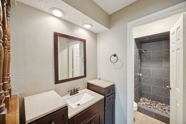 bathroom with tile patterned floors, a textured ceiling, toilet, tiled shower, and vanity