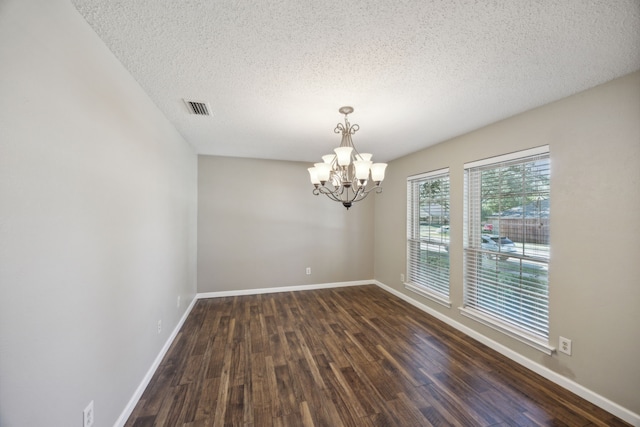 spare room with a textured ceiling, dark hardwood / wood-style floors, and a notable chandelier