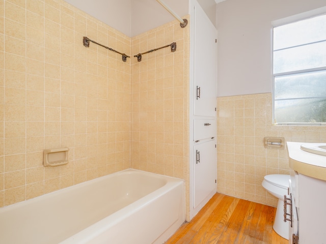 full bathroom featuring hardwood / wood-style floors, vanity, tiled shower / bath, toilet, and tile walls