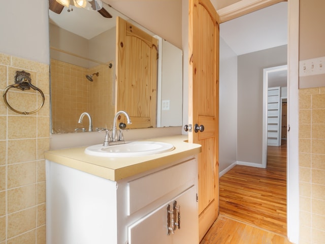 bathroom with hardwood / wood-style floors, vanity, ceiling fan, tile walls, and a tile shower