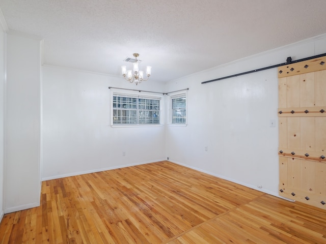 empty room featuring a textured ceiling, crown molding, wood-type flooring, a barn door, and an inviting chandelier