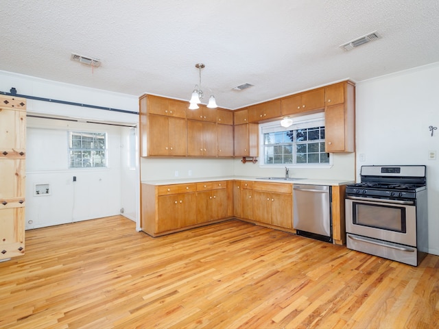 kitchen with hanging light fixtures, light hardwood / wood-style flooring, stainless steel appliances, and a textured ceiling