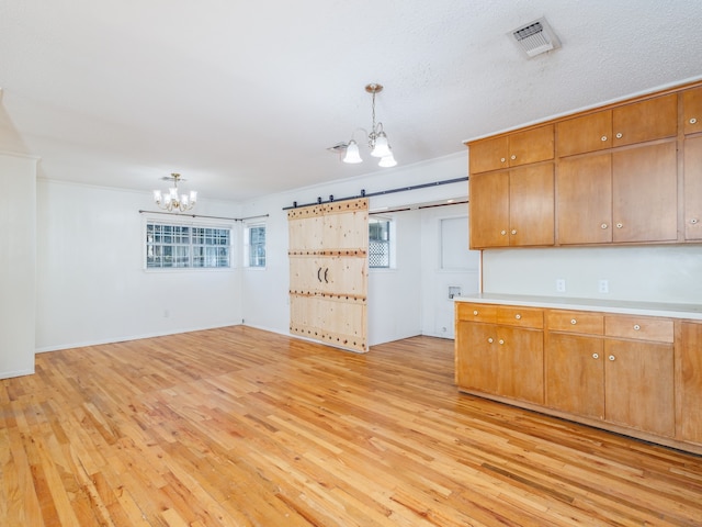 kitchen with light hardwood / wood-style flooring, a barn door, ornamental molding, decorative light fixtures, and a chandelier