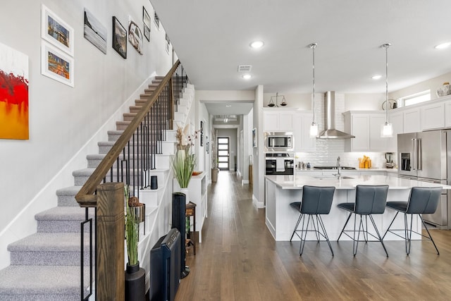 846 Belltown Dr, Allen, TX 75013 - kitchen with stainless steel appliances, wall chimney range hood, a kitchen bar, light countertops, and dark wood-type flooring