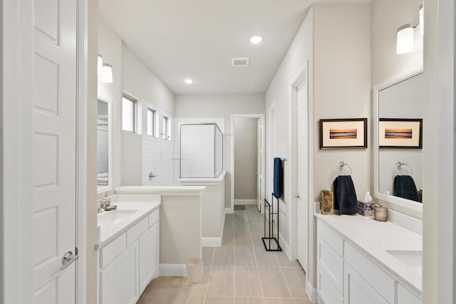 bathroom featuring two vanities, a sink, tile patterned flooring, baseboards, and walk in shower