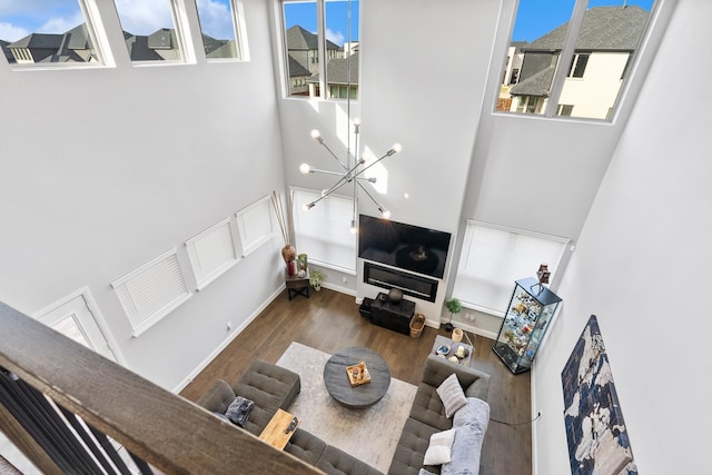 living area with a towering ceiling, baseboards, an inviting chandelier, and wood finished floors