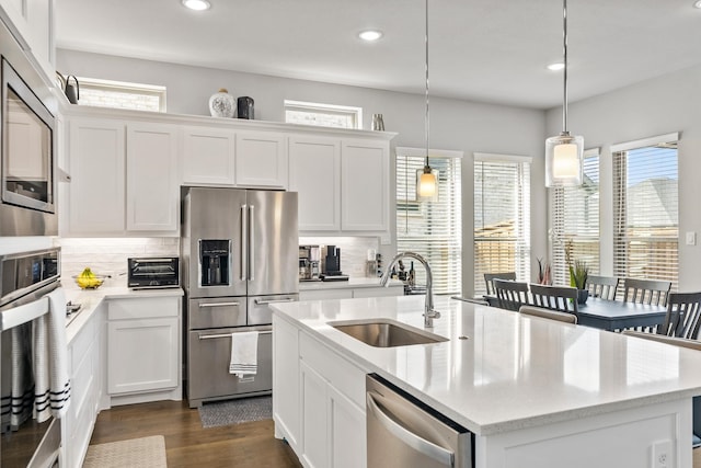 kitchen featuring appliances with stainless steel finishes, a kitchen island with sink, sink, white cabinets, and hanging light fixtures