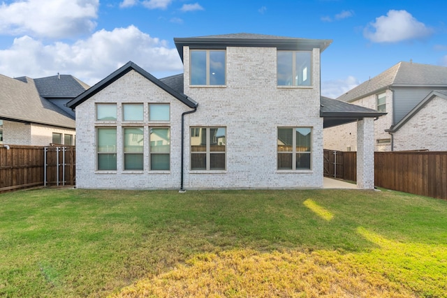 rear view of property featuring brick siding, a shingled roof, a lawn, a fenced backyard, and a patio area