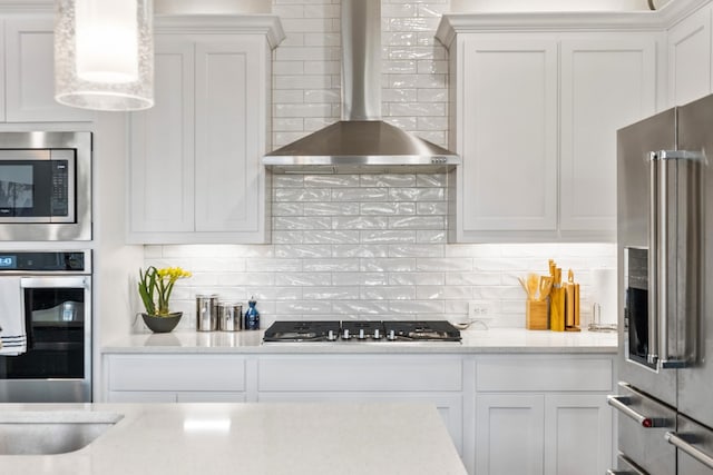 kitchen with backsplash, appliances with stainless steel finishes, white cabinetry, and wall chimney exhaust hood