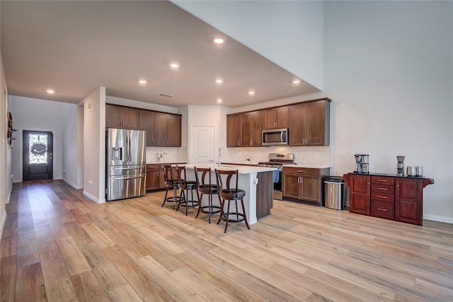 kitchen with stainless steel appliances, an island with sink, a breakfast bar area, decorative backsplash, and light wood-type flooring