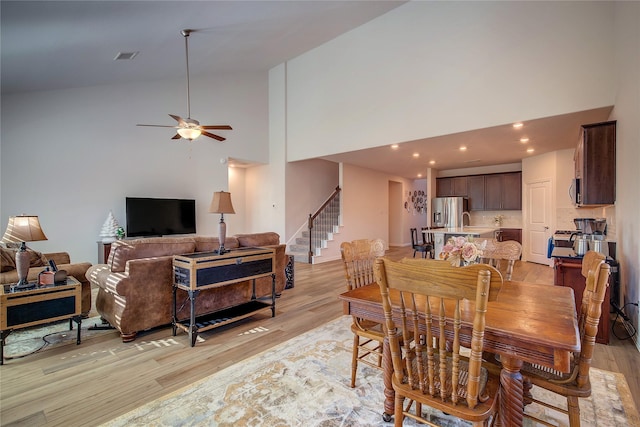 dining room with ceiling fan, light wood-type flooring, and high vaulted ceiling