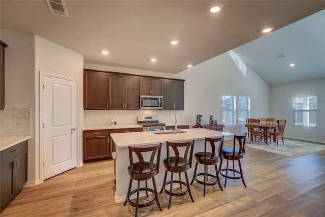 kitchen with appliances with stainless steel finishes, tasteful backsplash, light hardwood / wood-style flooring, and a kitchen island with sink