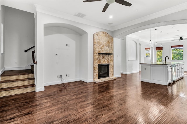 unfurnished living room with dark hardwood / wood-style floors, a fireplace, sink, ornamental molding, and ceiling fan