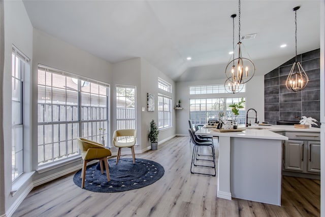 kitchen featuring sink, light hardwood / wood-style flooring, decorative light fixtures, vaulted ceiling, and a kitchen island