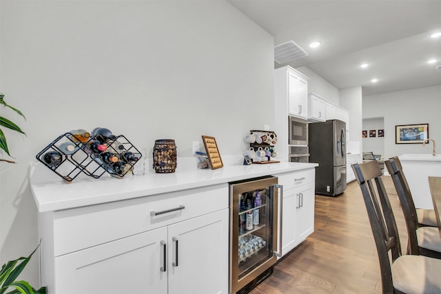 kitchen with sink, beverage cooler, stainless steel appliances, dark hardwood / wood-style flooring, and white cabinets