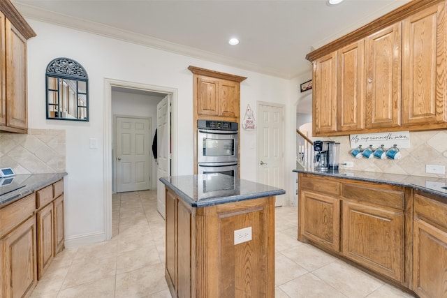 kitchen featuring a center island, stainless steel double oven, tasteful backsplash, dark stone countertops, and crown molding