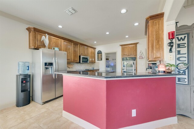 kitchen with crown molding, light tile patterned floors, stainless steel appliances, and an island with sink