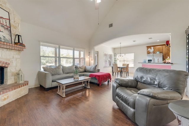 living room with dark hardwood / wood-style flooring, high vaulted ceiling, a stone fireplace, and ceiling fan