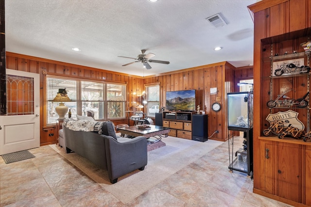 living room featuring a textured ceiling, ceiling fan, and wood walls