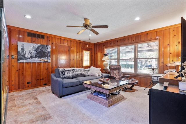 living room featuring a textured ceiling, ceiling fan, and wooden walls