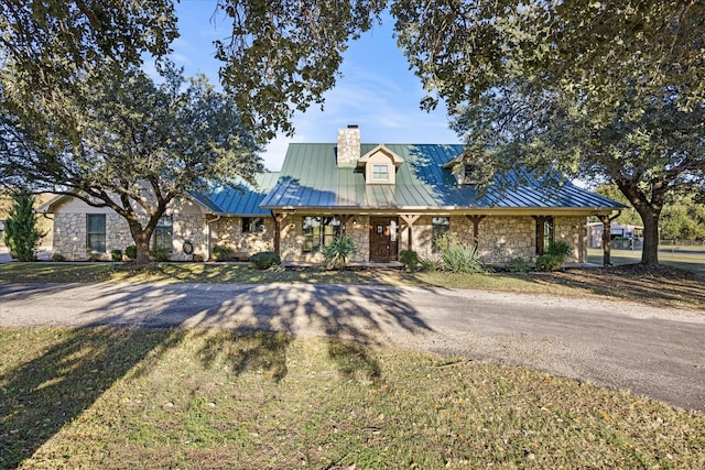 view of front of home with metal roof, stone siding, driveway, and a standing seam roof