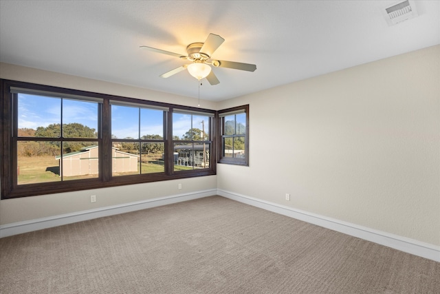 carpeted empty room with a ceiling fan, plenty of natural light, baseboards, and visible vents