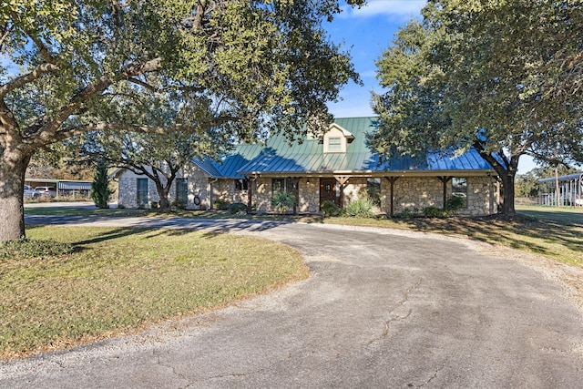 view of front of house featuring a front lawn, a standing seam roof, aphalt driveway, stone siding, and metal roof