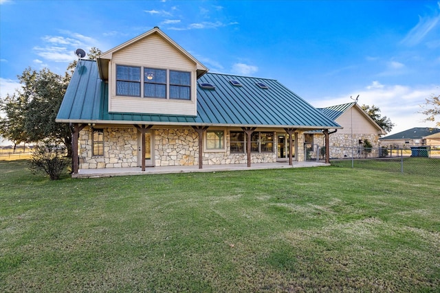 rear view of house featuring a standing seam roof, stone siding, fence, a yard, and metal roof