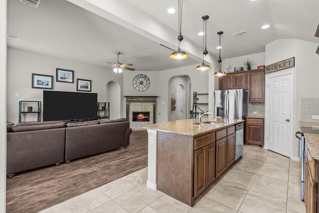 kitchen featuring sink, stainless steel appliances, an island with sink, pendant lighting, and a fireplace