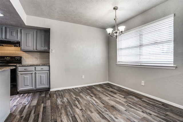 unfurnished dining area with dark hardwood / wood-style flooring, a textured ceiling, and an inviting chandelier