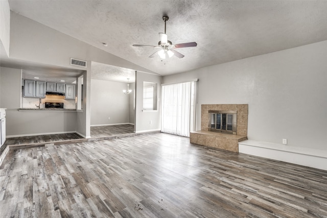 unfurnished living room featuring dark wood-type flooring, ceiling fan with notable chandelier, vaulted ceiling, a textured ceiling, and a tiled fireplace